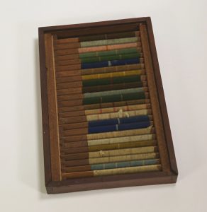 Photograph of a wooden box containing 24 wooden cards. Each card is wrapped in a different color of yarn with varying striped patterns.